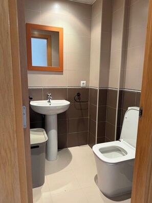 A bathroom with a sink, mirror, toilet, and trash bin. - Vrbo Property (Cancelada)