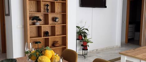 Een eetgedeelte met een houten tafel voor vier personen, omringd door stoelen. Achtergrond toont een grote houten boekenkast met diverse decoratieve objecten.