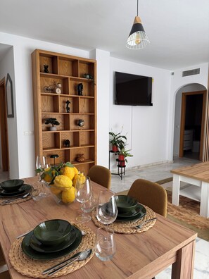 A dining area with a wooden table set for four, surrounded by chairs. A large wooden bookshelf with various decorative items is visible in the background. - Vrbo Property (Cancelada)