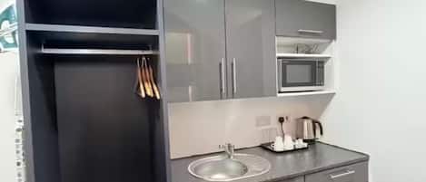 A compact kitchenette with a microwave, sink, and a small cabinet.