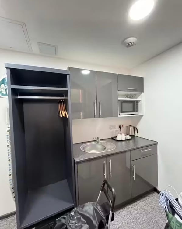 Una kitchenette compacta con microondas, pileta y un mueble pequeño.