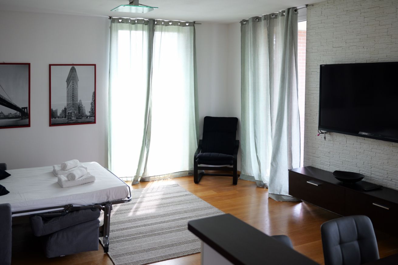 Ein Hotelzimmer mit einem Bett, einem Sessel, einem Fernseher und einem Fenster mit Vorhängen.