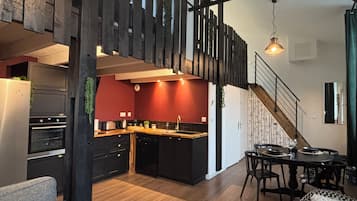 A modern kitchen with a red backsplash, wooden flooring, and a dining area with a table and chairs.