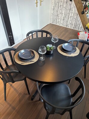 Ett runt matbord med svarta stolar, en liten krukväxt och två vinglas.