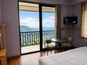 Een hotelkamer met een bed, een tafel met stoelen, een televisie en een balkon met uitzicht op de bergen.