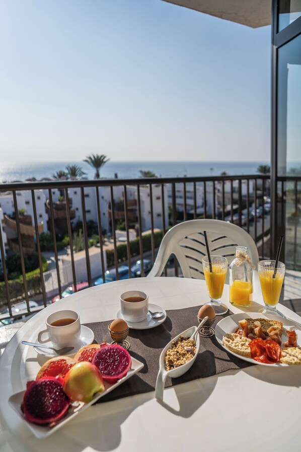 A balcony table with breakfast items, a view of the sea, and a cityscape in the background. - Guinea Apartments (San Bartolomé de Tirajana)