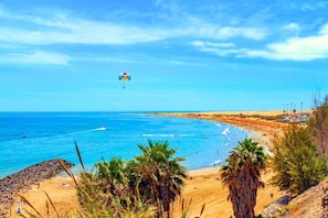 Una playa con cielos despejados, una orilla arenosa y una cometa volando.