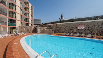 Una piscina con lettini e una parete in pietra.