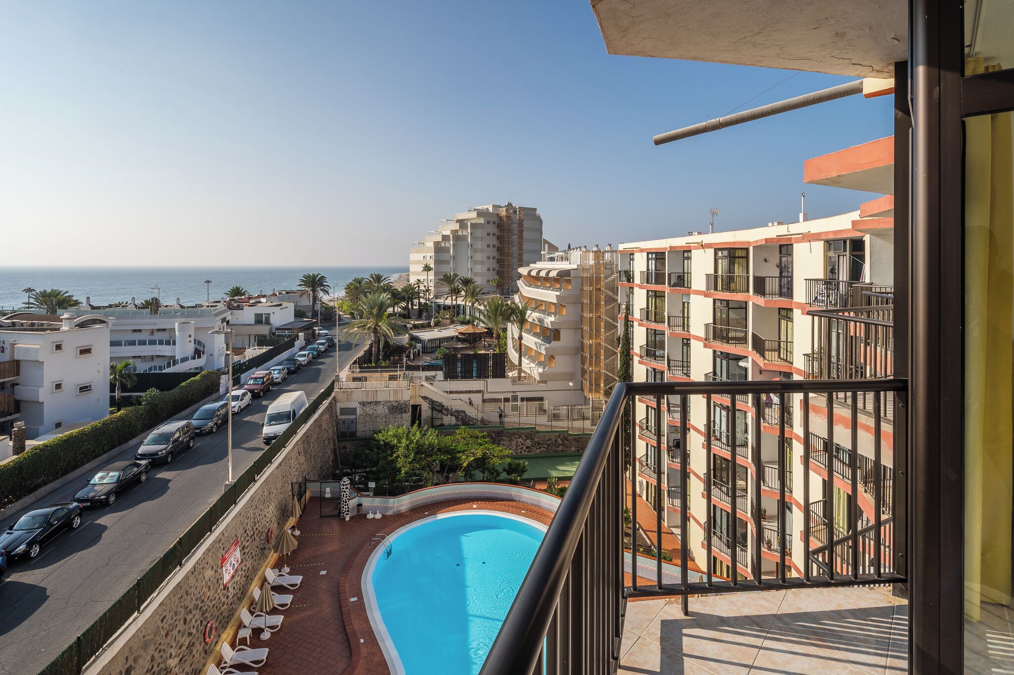 A residential building with a swimming pool, a street with parked cars, and a view of the sea.