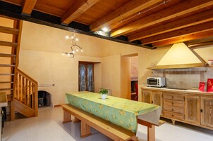 Una cocina con armarios de madera, un microondas y una mesa con mantel estampado de frutas.