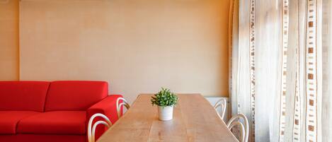 A room with a wooden dining table, a red sofa, white chairs, and a potted plant.