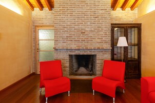 Una habitación con chimenea de ladrillo, vigas de madera y sillas rojas.