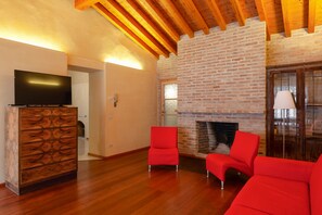 Una sala de estar con un televisor sobre un mueble de madera, una chimenea de ladrillo y sillas rojas.