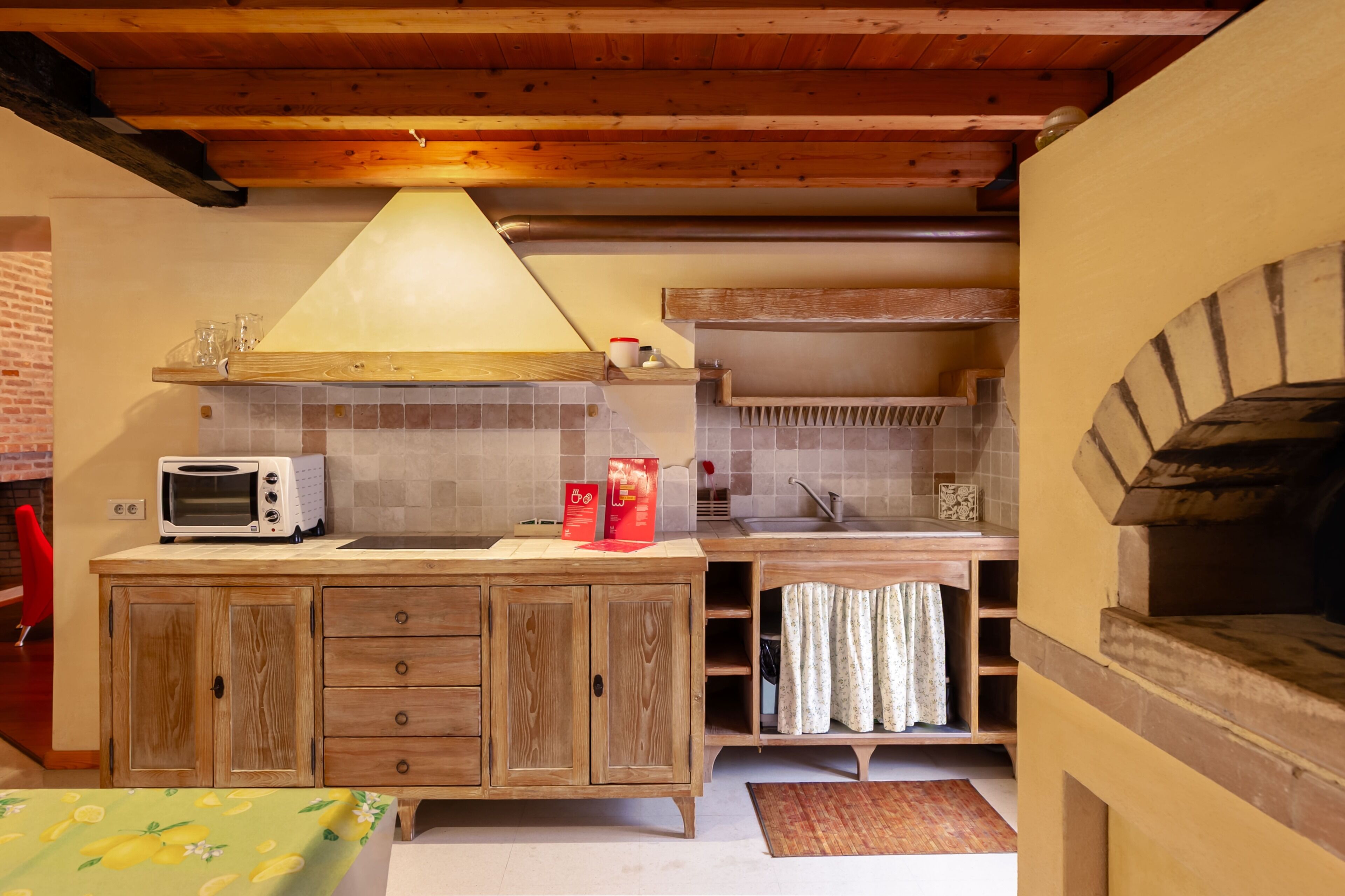 A compact kitchen with wooden cabinets, a microwave, a hanging light fixture, and a built-in oven.