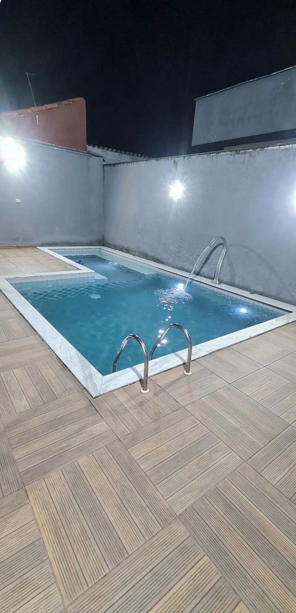 A rectangular outdoor swimming pool with two metal ladders on one side, surrounded by a tiled deck.