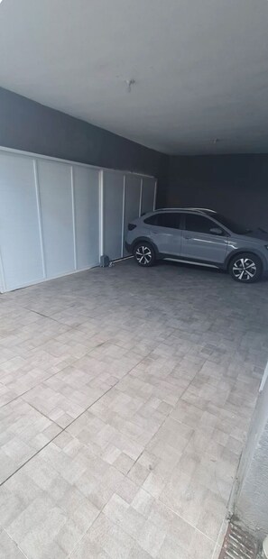 A car parked in a covered parking area with a tiled floor and a grey wall. - Great house in Itanhaém (Itanhaém)