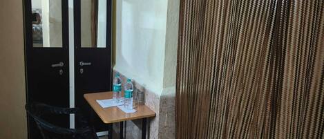 A small room with a desk, two water bottles, a chair, and a black wardrobe.