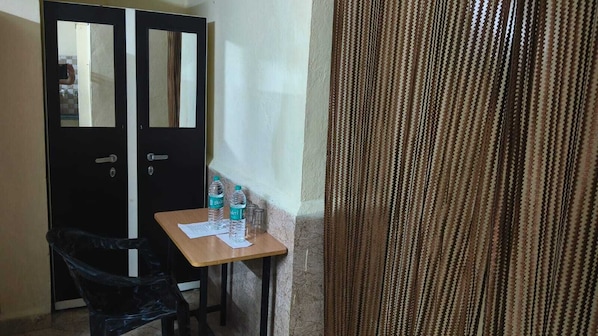 A small room with a desk, two water bottles, a chair, and a black wardrobe.