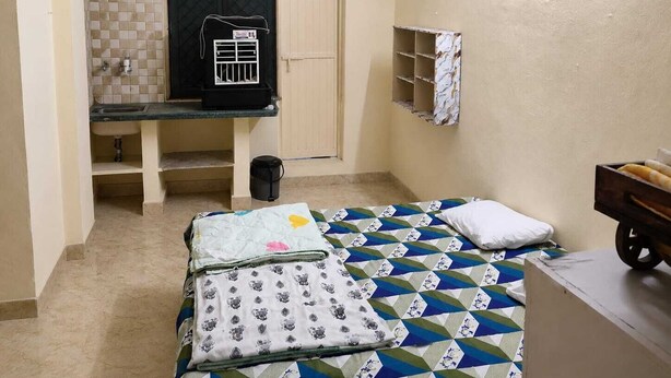 Une petite chambre comprenant un lit, un petit bureau, un radiateur et une étagère avec une serviette.