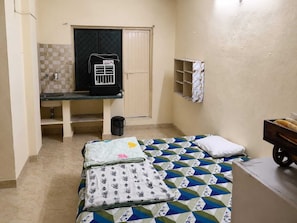 A compact room with a bed, a small desk, a radiator, and a shelf with a towel.