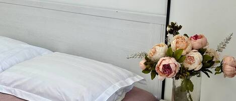 A bedroom with a bed, a nightstand with drawers, and a vase with flowers.