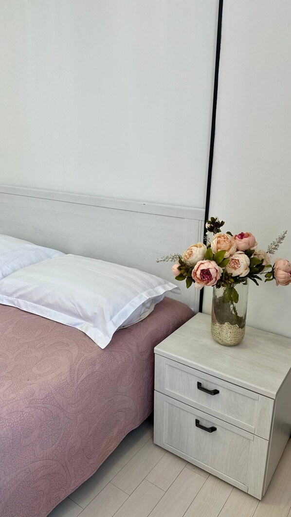 A bedroom with a bed, a nightstand with drawers, and a vase with flowers.