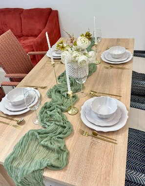 A dining table set with white plates, gold cutlery, and a green cloth runner.