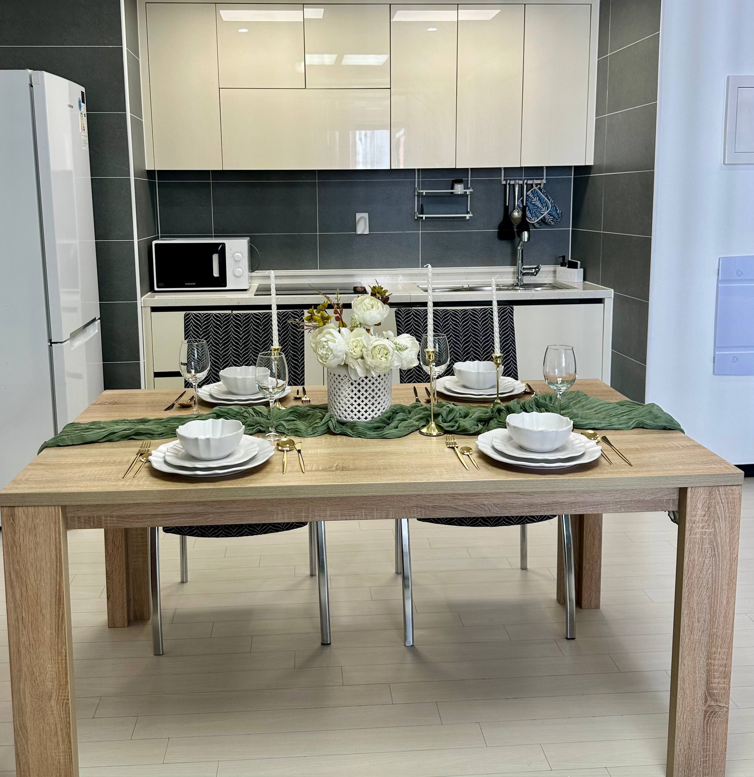 A modern kitchen with a dining table set for four, featuring a white and green color scheme, stainless steel appliances, and a herringbone patterned backsplash.