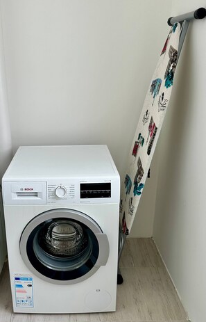 A white Bosch washing machine in a corner with a patterned curtain.