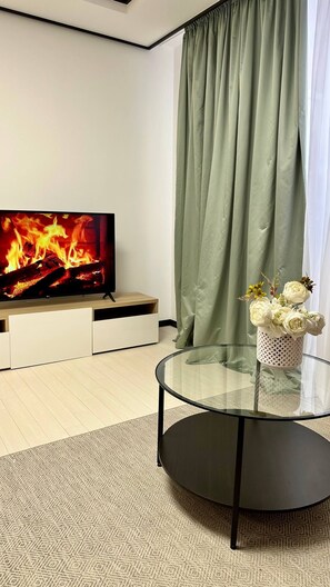 A modern living room with a flat-screen TV, a glass coffee table, and a decorative vase with flowers.
