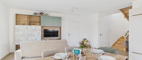 Un comedor con una mesa de madera dispuesta para cuatro personas, un sofá y un televisor montado en la pared.