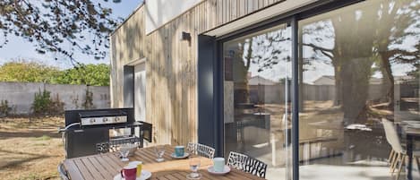 Un espace extérieur aménagé pour les repas, avec une table en bois, des chaises et un barbecue.