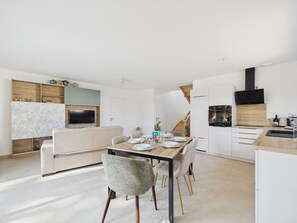 A modern kitchen with a built-in oven, a dining area with a wooden table and chairs, and a living area with a sofa and a television. - Fully equipped house for 6 with garden (Saint-Hilaire-de-Riez)