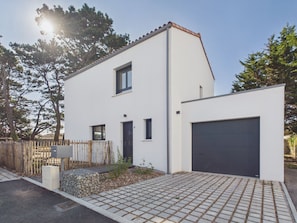 A modern two-story house with a garage, a small front yard with a stone planter, and a wooden fence. - Fully equipped house for 6 with garden (Saint-Hilaire-de-Riez)