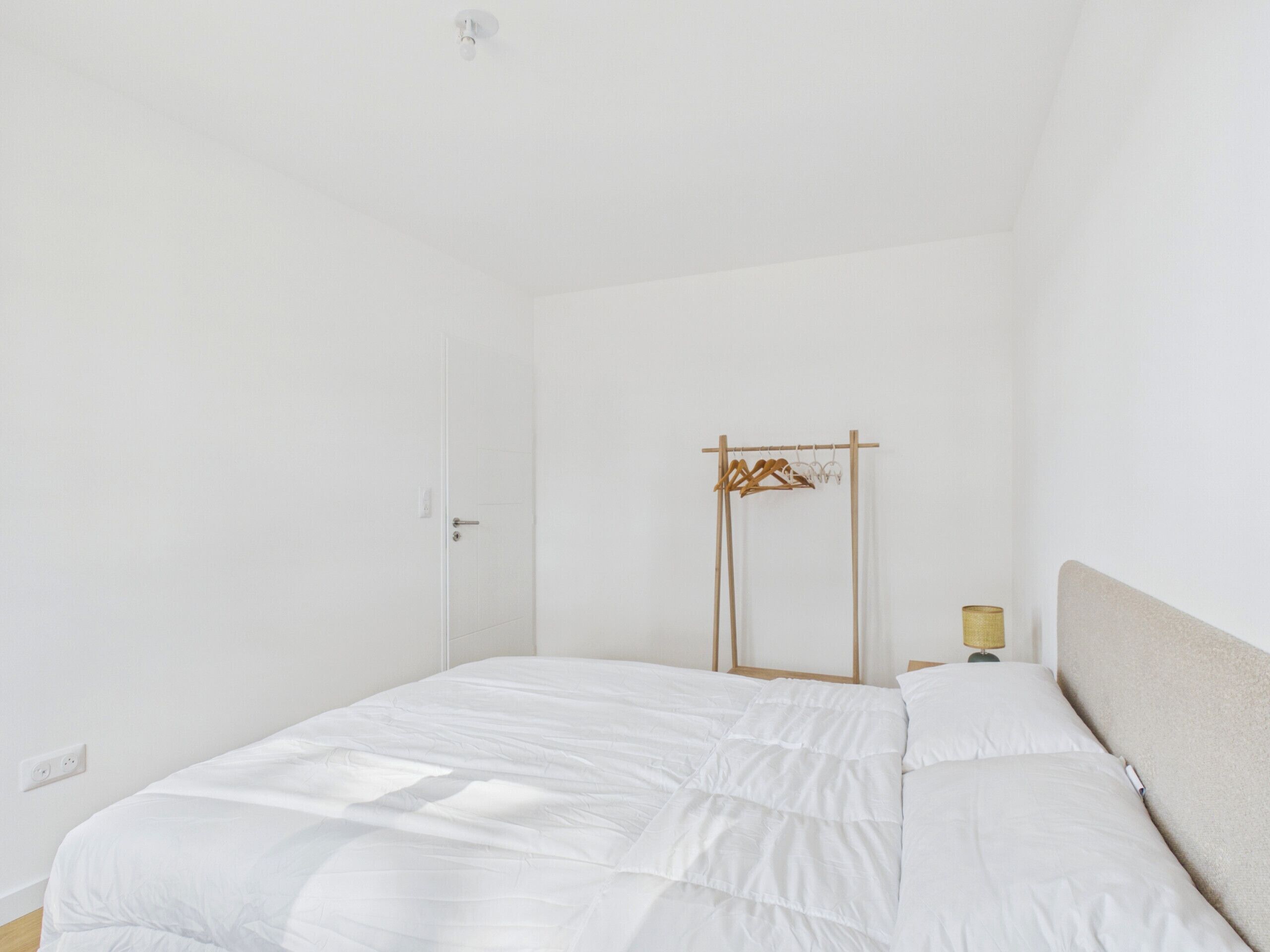 A minimalist bedroom with a bed, a hanging clothes rack, and a bedside lamp.