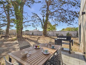 Eine Terrasse im Freien mit einem Holztisch, gedeckt für ein Essen, einem Grill und Blick auf eine Wohngegend.