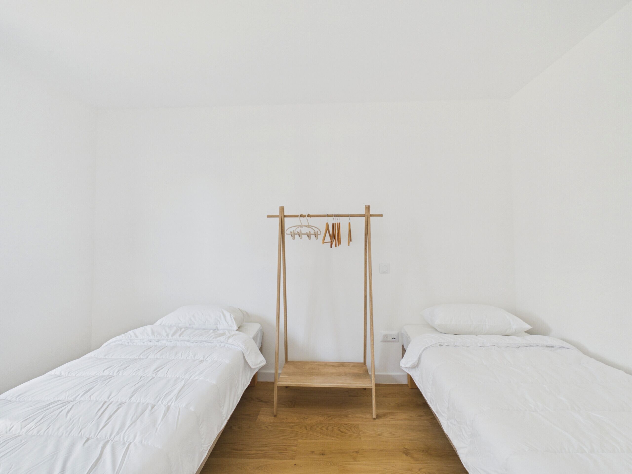 Habitación minimalista con dos camas individuales, un armario de madera y una pared blanca sencilla.