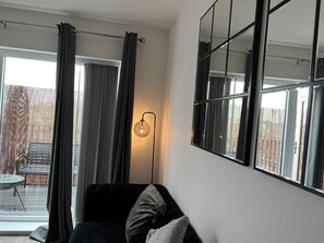 Een moderne zithoek met een zwarte bank, een glazen tafel en een vloerlamp.