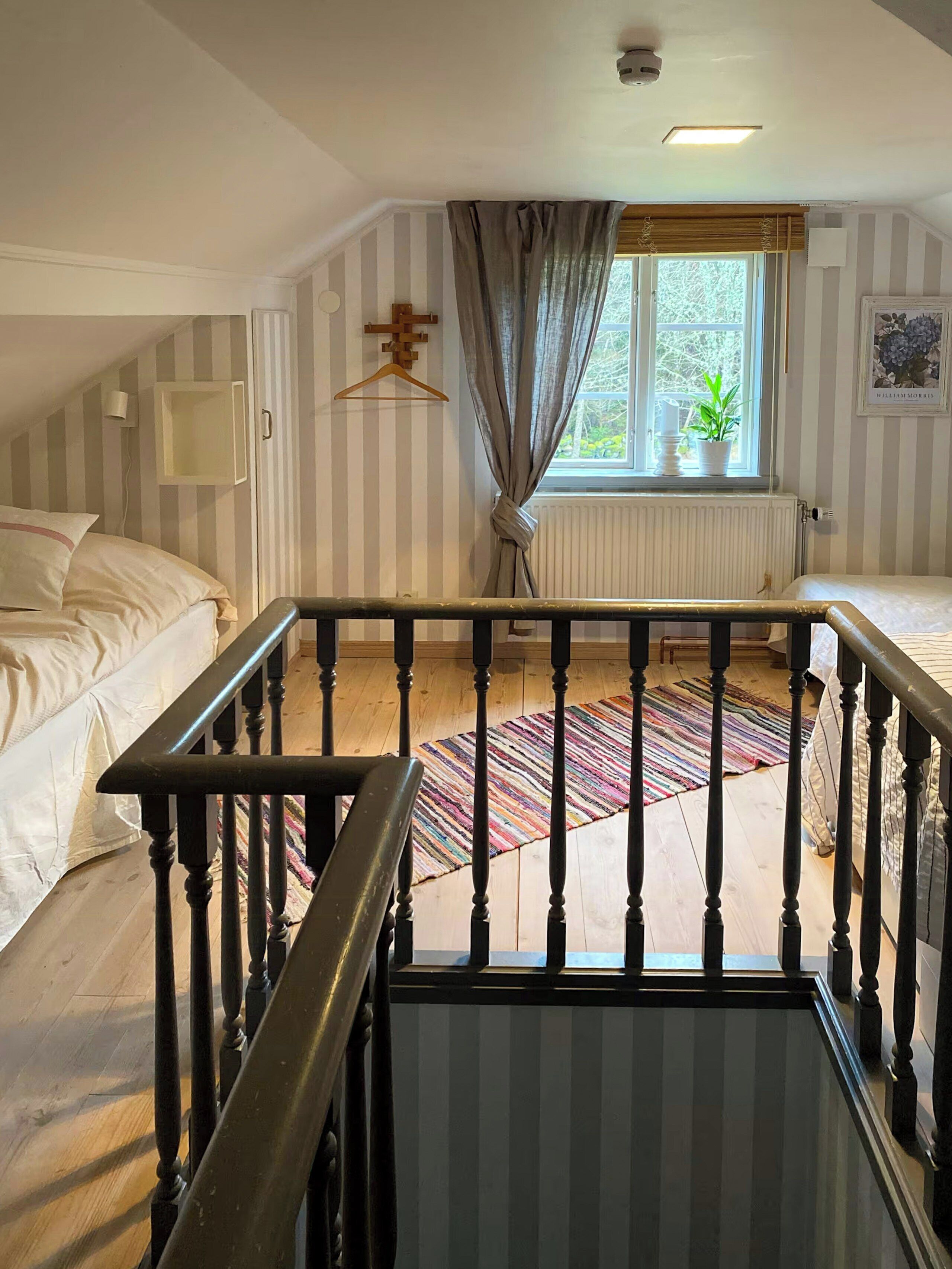 A room with a bed, a window with curtains, a radiator, a hanging light, and a wooden floor.