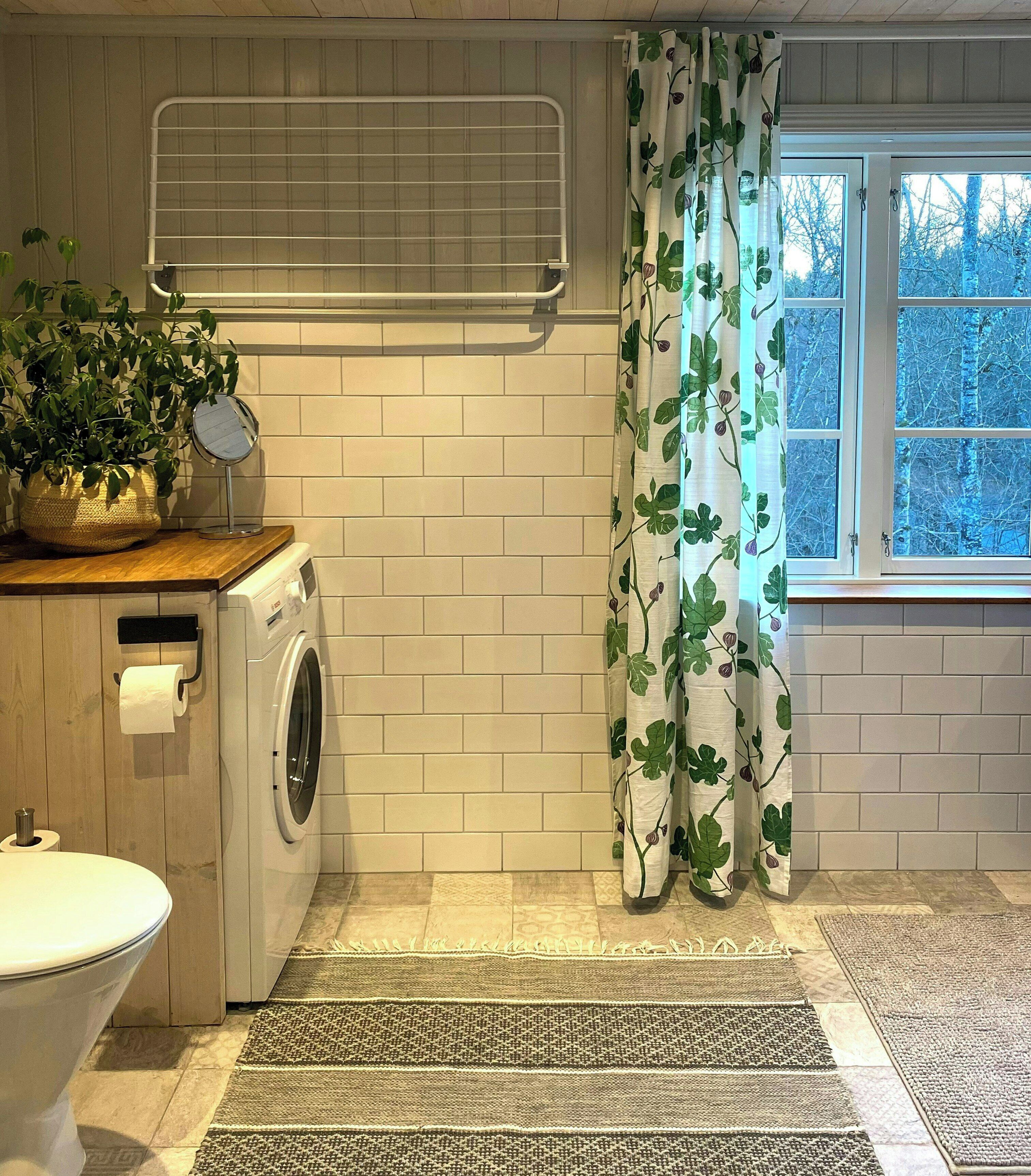 Une buanderie équipée d’un lave-linge, d’un étendoir, de toilettes et d’une fenêtre donnant sur les arbres.