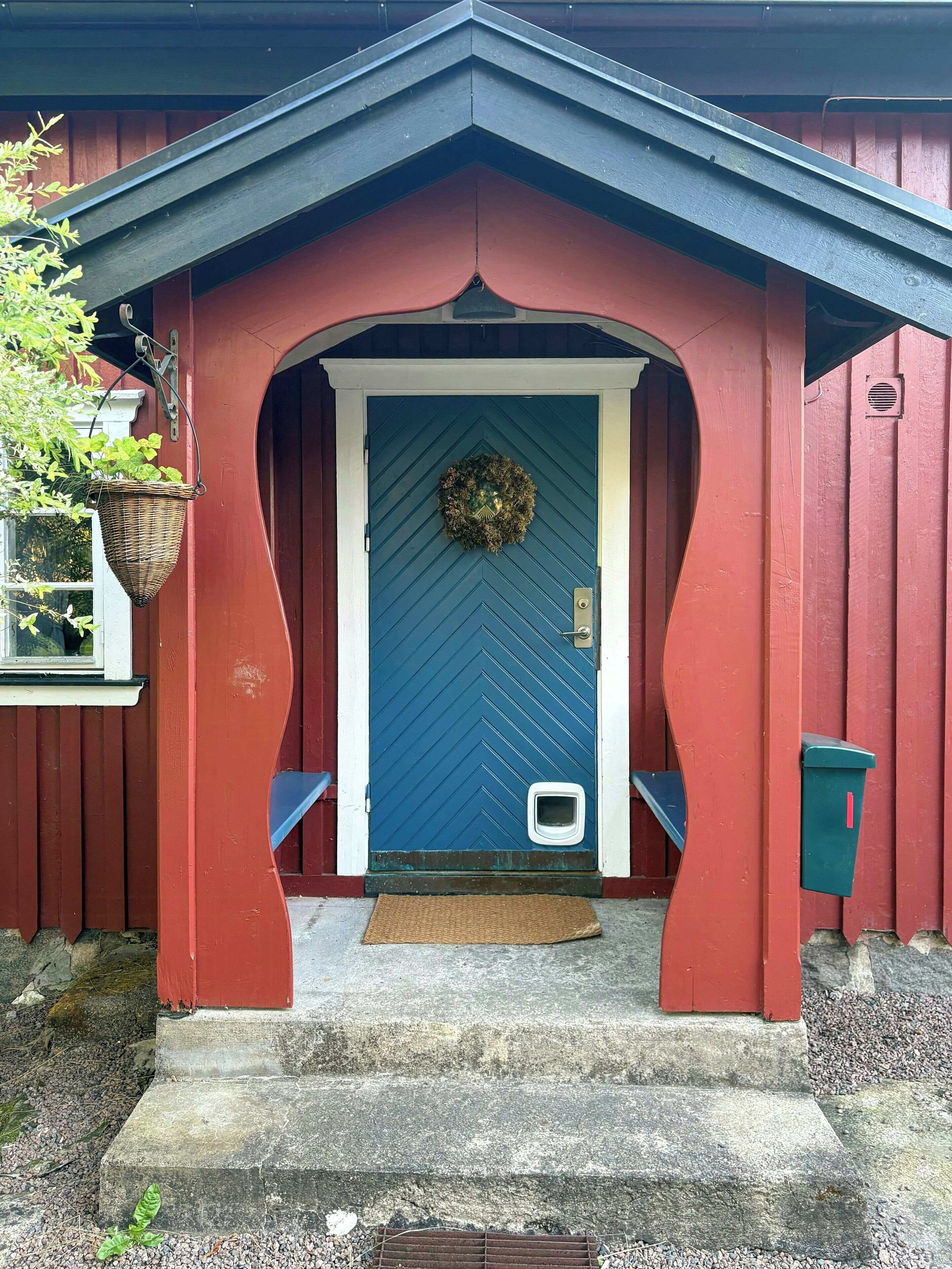 A red and blue house with a blue door, a small mailbox, and a hanging basket.