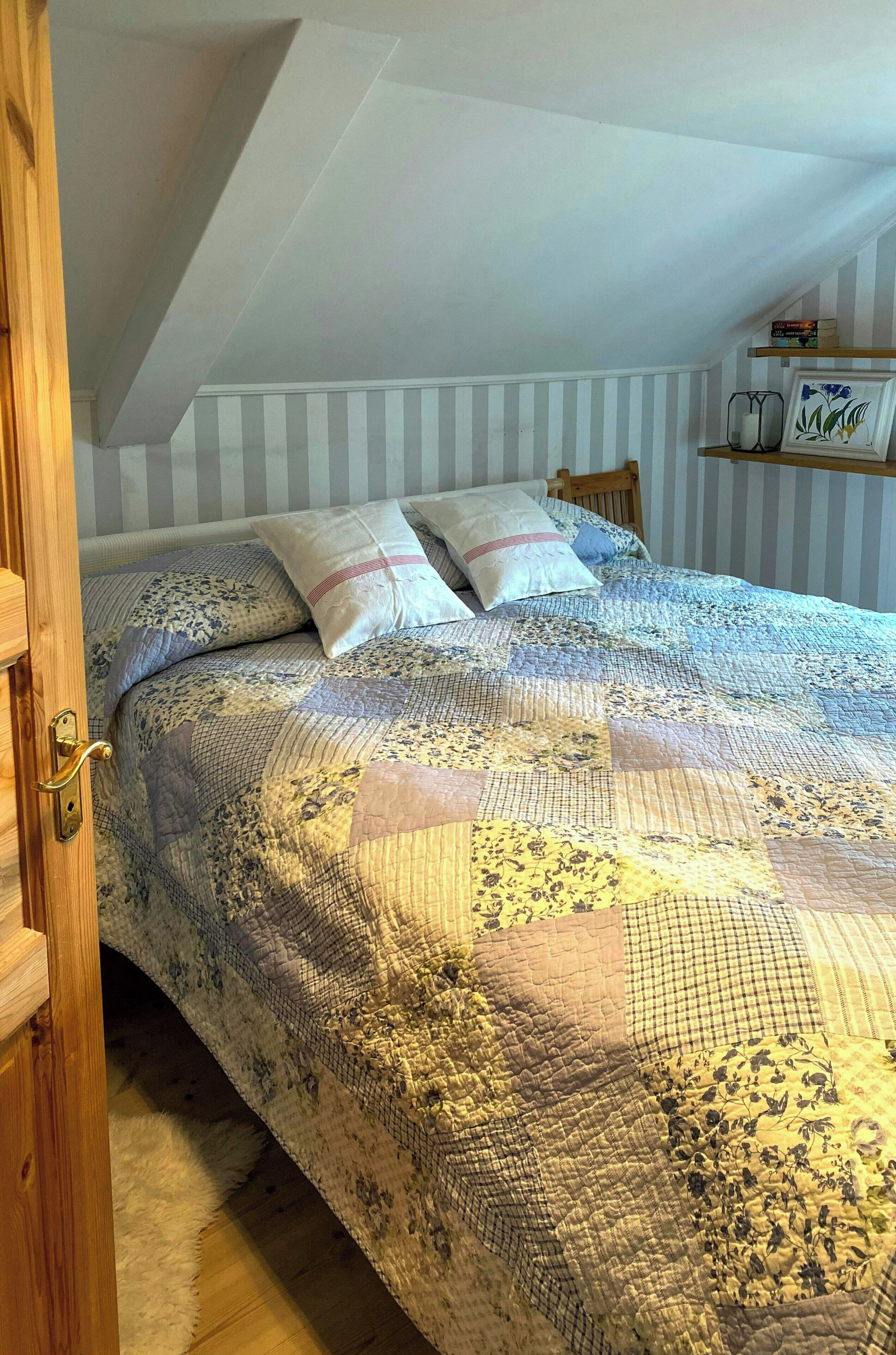 A bedroom with a quilted bedspread, striped wallpaper, and a wooden door.