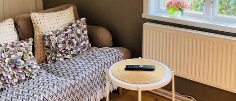 A cozy room with a sofa, a small round table, and a window with a view of greenery.