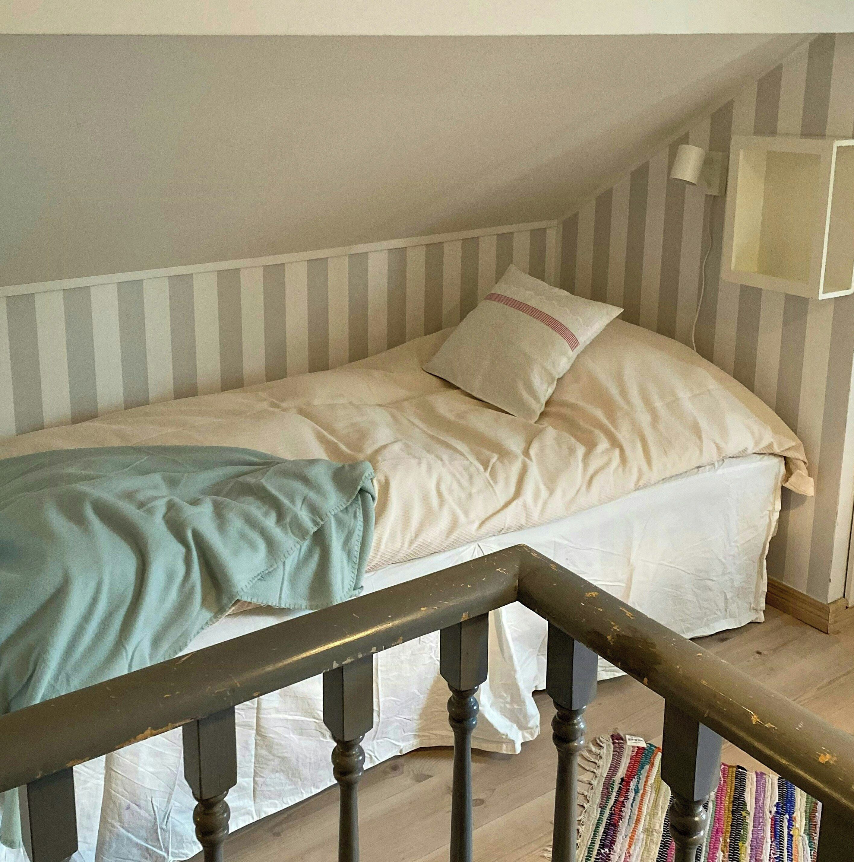 A single bed with a striped headboard, a bedside lamp, and a colorful rug on a wooden floor.