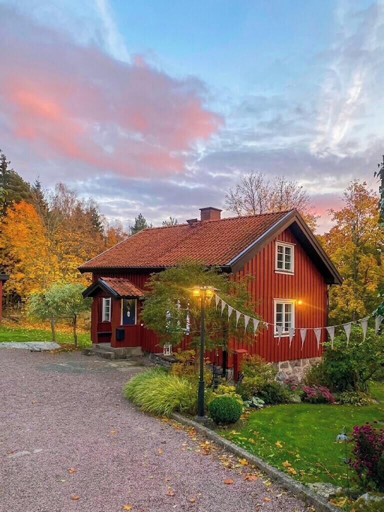 A red wooden house with a gravel driveway and a well-maintained garden.