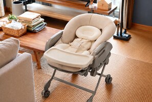 A baby stroller with a tray, wheels, and a cushioned seat, placed in a room with a wooden floor and a bench in the background.