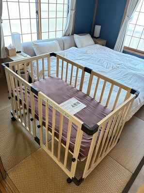 A room with a bed, a crib, a nightstand, and a window with curtains.