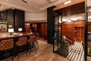 A bar area with stools, a bar counter, and a view of a staircase leading to a lower level. - Steps to Powell’s & Art Museum | Pet-friendly. Gym (Portland)