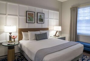 Une chambre d’hôtel avec un grand lit, deux tables de chevet avec des lampes, une tête de lit et deux tableaux encadrés accrochés au mur.