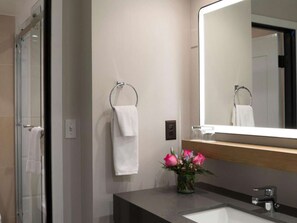 Une salle de bain moderne avec une douche à parois de verre, un lavabo avec un miroir et un vase rempli de fleurs.
